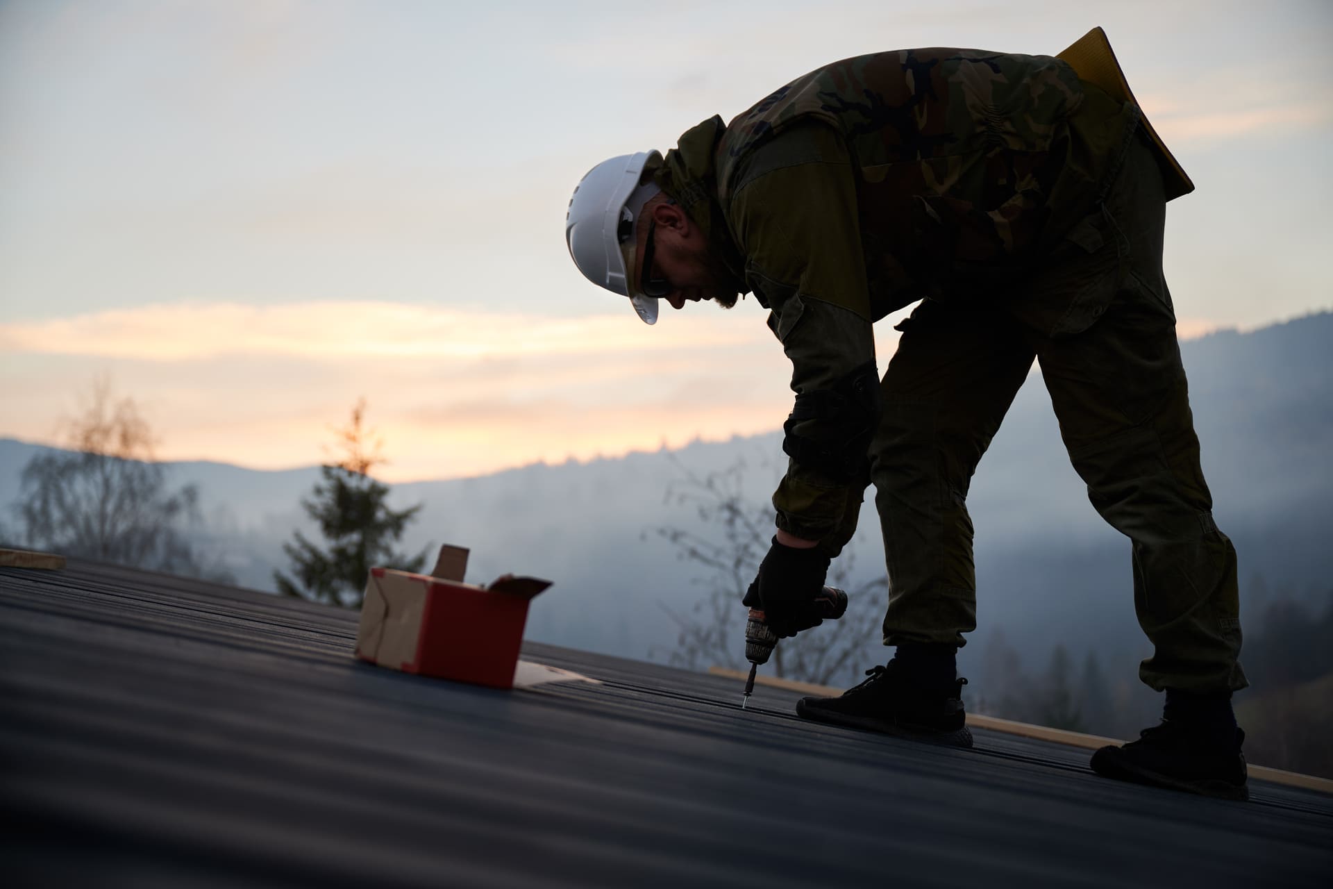 man-drilling-on-metal-roof-at-sunset