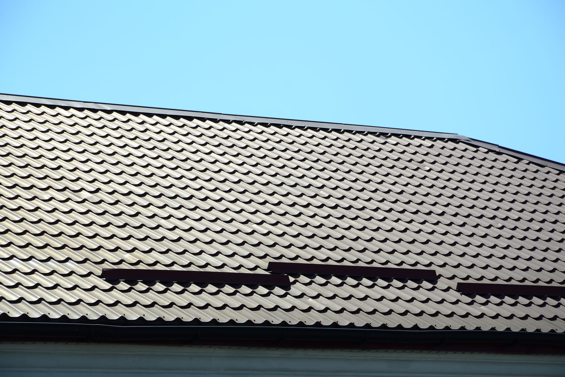 dark-red-metal-tile-roof-against-clear-blue-sky