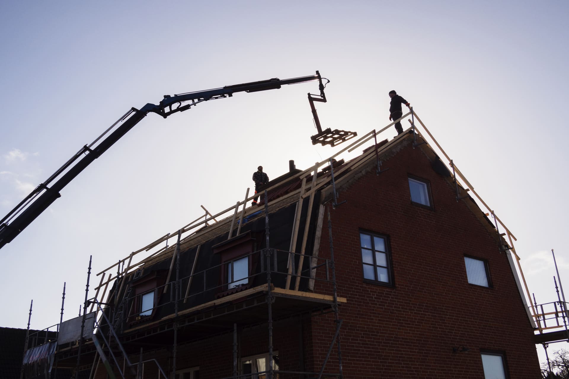 silhouette-of-workers-on-house-roof-with-crane-lifting-materials