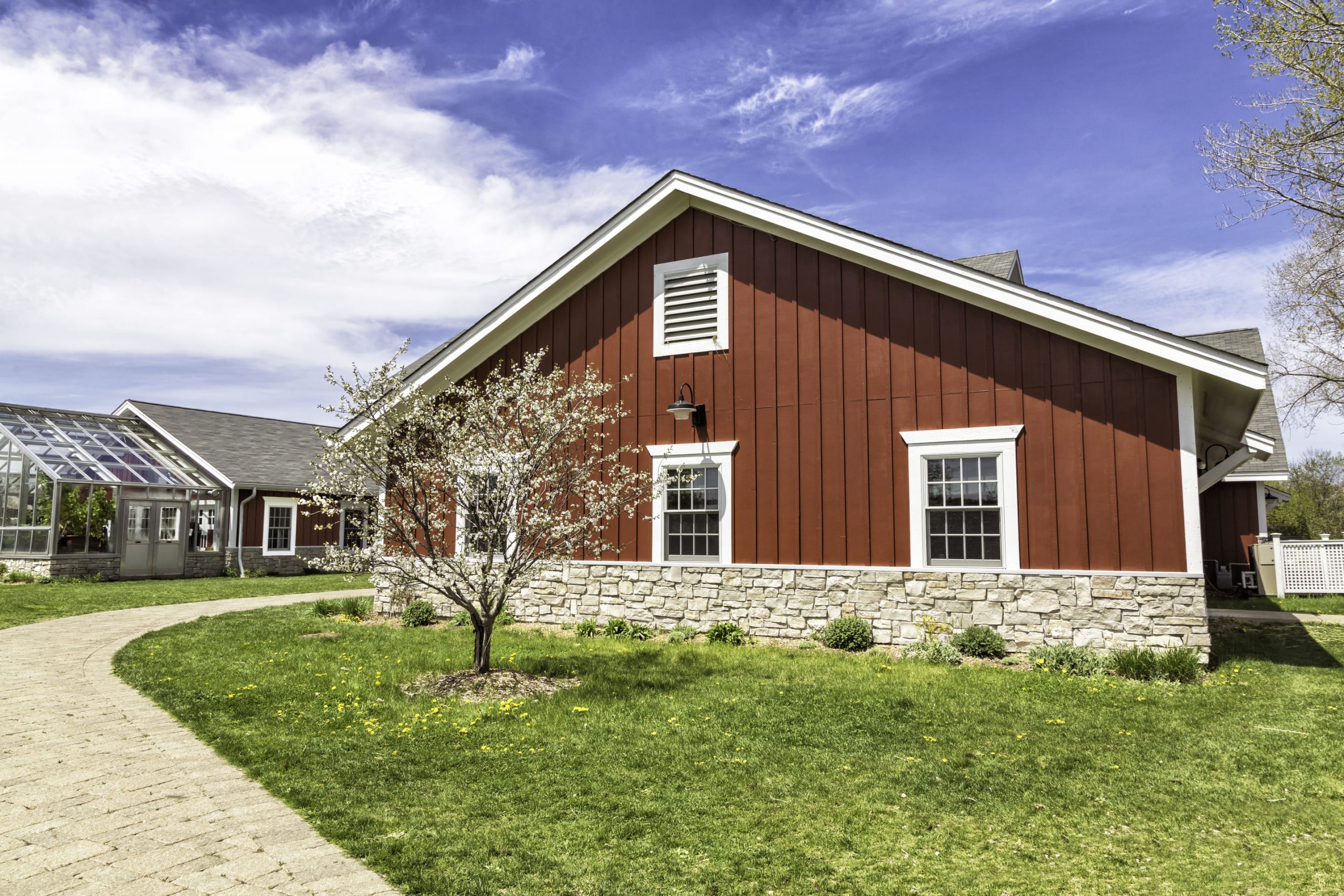 red-barn-style-house-with-stone-foundation-and-greenhouse-under-blue-sky