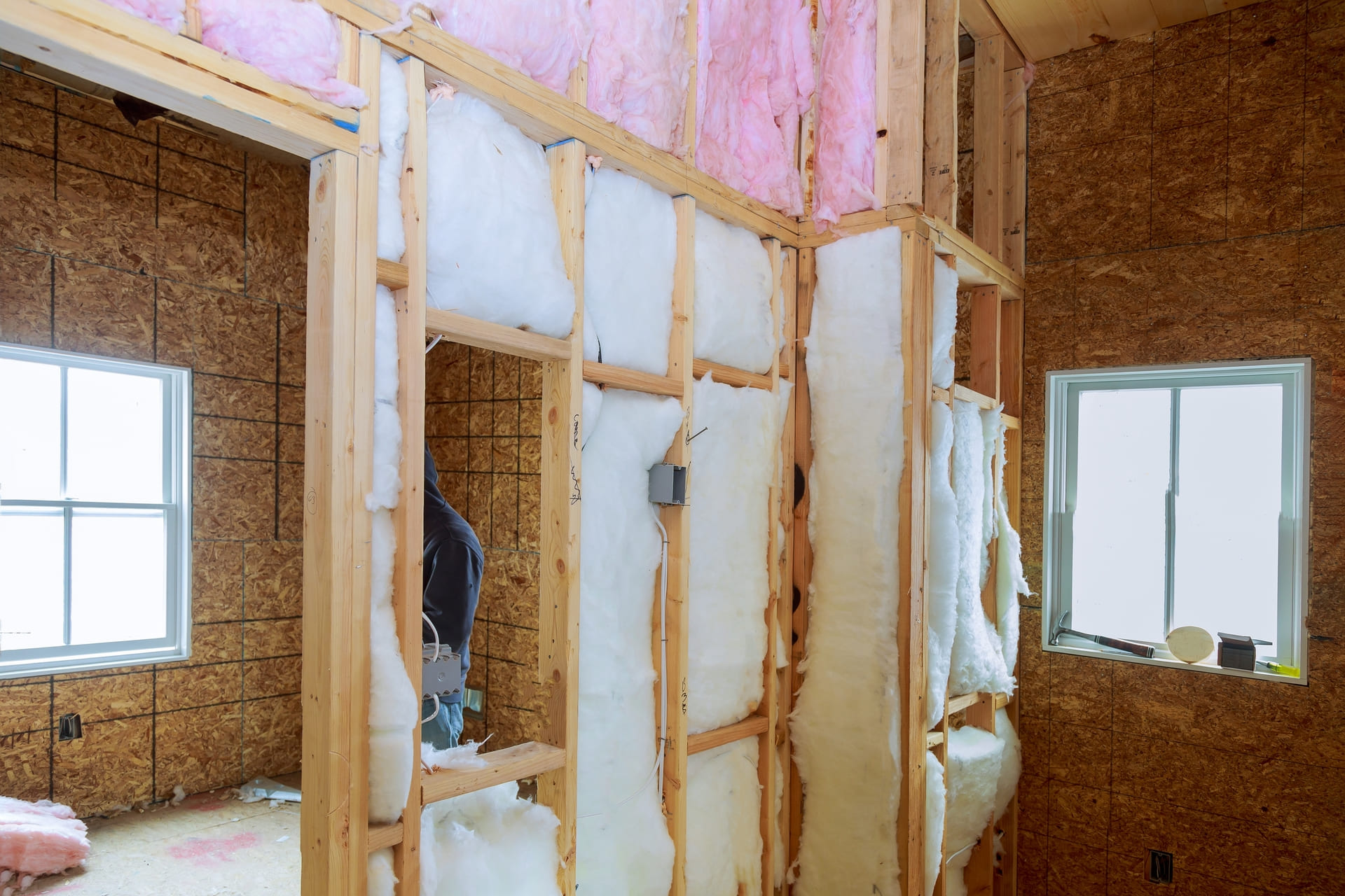 contractor-installing-white-and-pink-insulation-between-wooden-wall-studs-in-unfinished-room